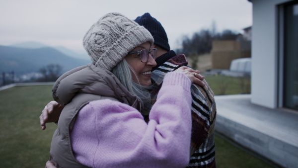 A senior man hugging and consoling his wife outdoors in garden in winter.