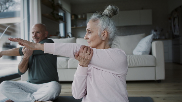 A senior couple doing relaxation exercise together at home.