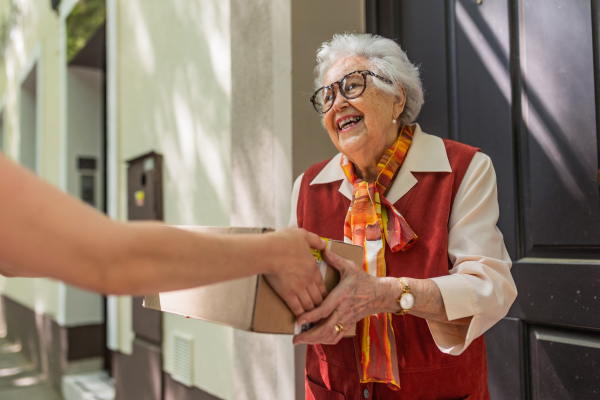 Elderly woman in front of her house, picking up package from the courier.