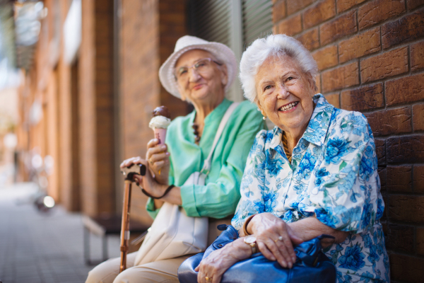 Portrait of two senior female friends in the city, eating ice cream on a hot summer day. Elderly ladies on summer vacation in the city. Pensioners on group trip. Concept of senior vacation and travel groups, clubs.