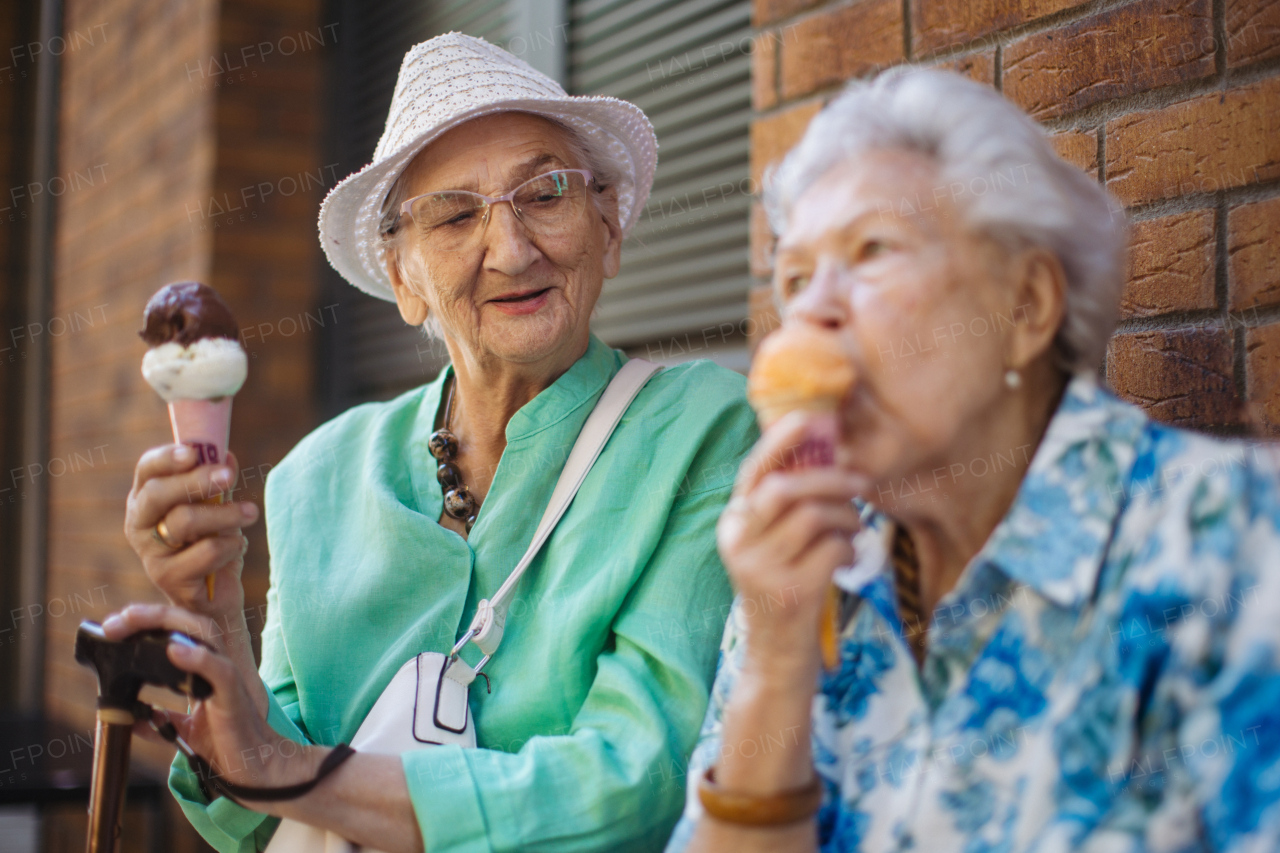 Portrait of two senior female friends in the city, eating ice cream on a hot summer day. Elderly ladies on summer vacation in the city. Pensioners on group trip. Concept of senior vacation and travel groups, clubs.