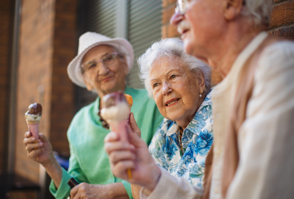 Portrait of three senior friends in the city, eating ice cream on a hot summer day. Elderly ladies on summer vacation in the city. Pensioners on group trip. Concept of senior vacation and travel groups, clubs.