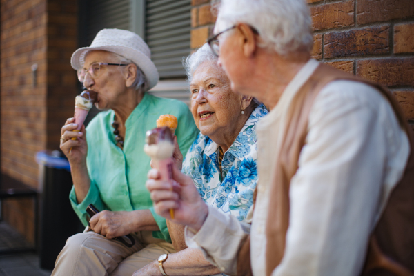 Portrait of three senior friends in the city, eating ice cream on a hot summer day. Elderly ladies on summer vacation in the city. Pensioners on group trip. Concept of senior vacation and travel groups, clubs.