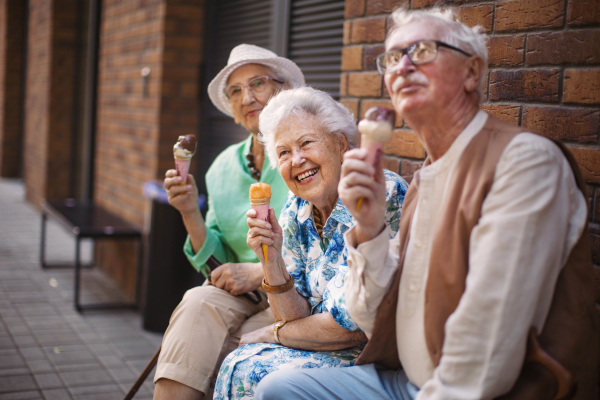 Portrait of three senior friends in the city, eating ice cream on a hot summer day. Elderly ladies on summer vacation in the city. Pensioners on group trip. Concept of senior vacation and travel groups, clubs.