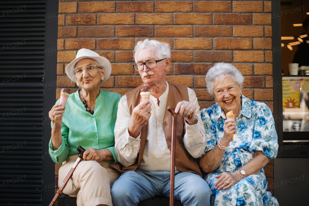 Portrait of three senior friends in the city, eating ice cream on a hot summer day. Elderly ladies on summer vacation in the city. Pensioners on group trip. Concept of senior vacation and travel groups, clubs.