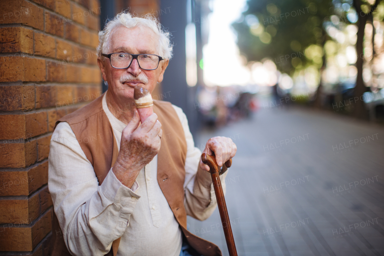 Portrait of senior man with walking cane, eating ice cream on a hot summer day in the city. Elderly tourist on summer vacation in the city.