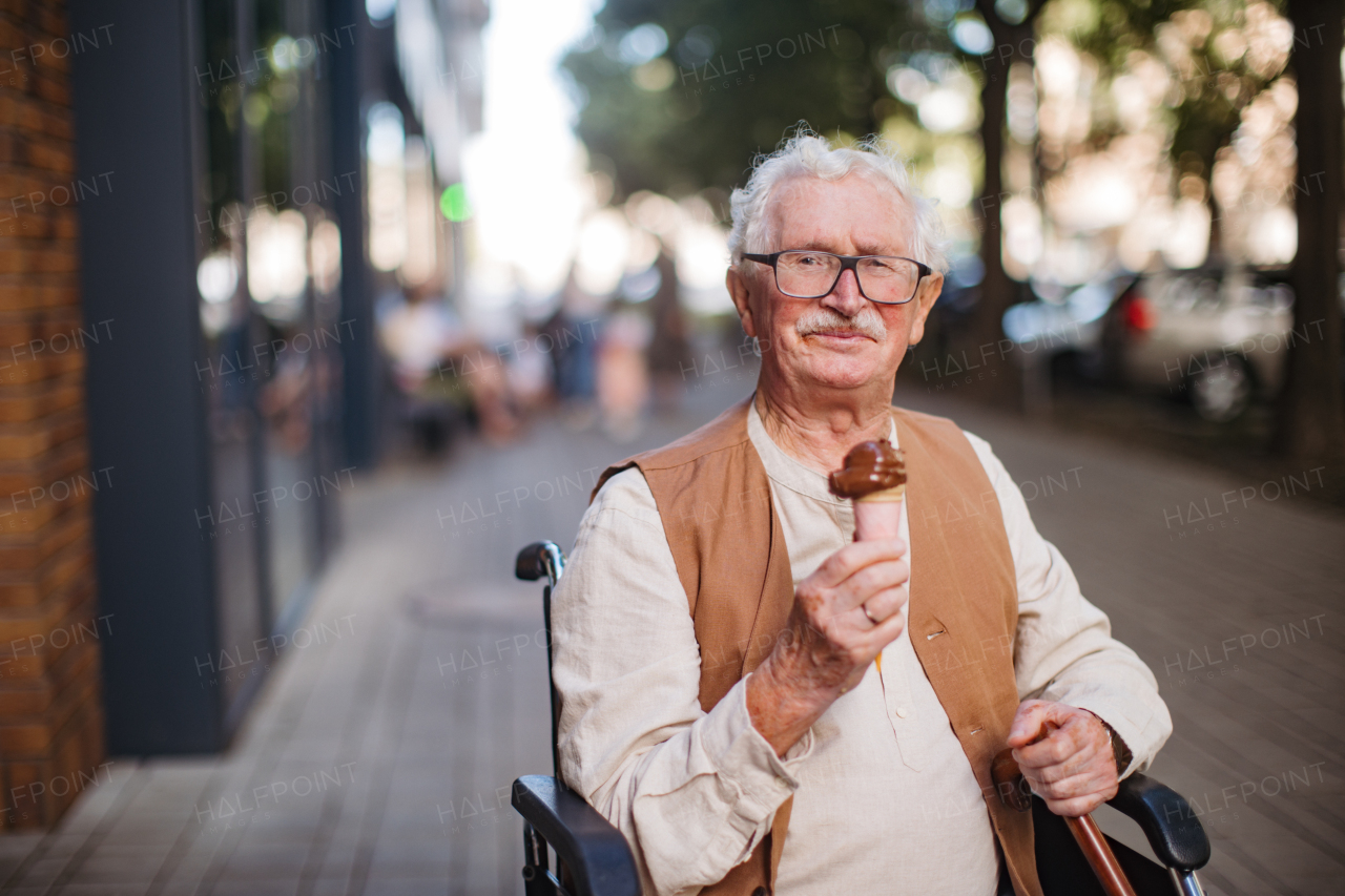 Portrait of senior man on wheelchair, eating ice cream on a hot summer day in the city. Elderly tourist on summer vacation in the city.