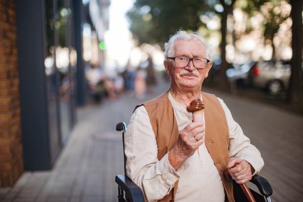 Portrait of senior man on wheelchair, eating ice cream on a hot summer day in the city. Elderly tourist on summer vacation in the city.