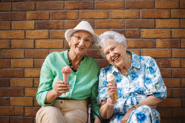 Portrait of two senior female friends in the city, eating ice cream on a hot summer day. Elderly ladies on summer vacation in the city. Pensioners on group trip. Concept of senior vacation and travel groups, clubs.