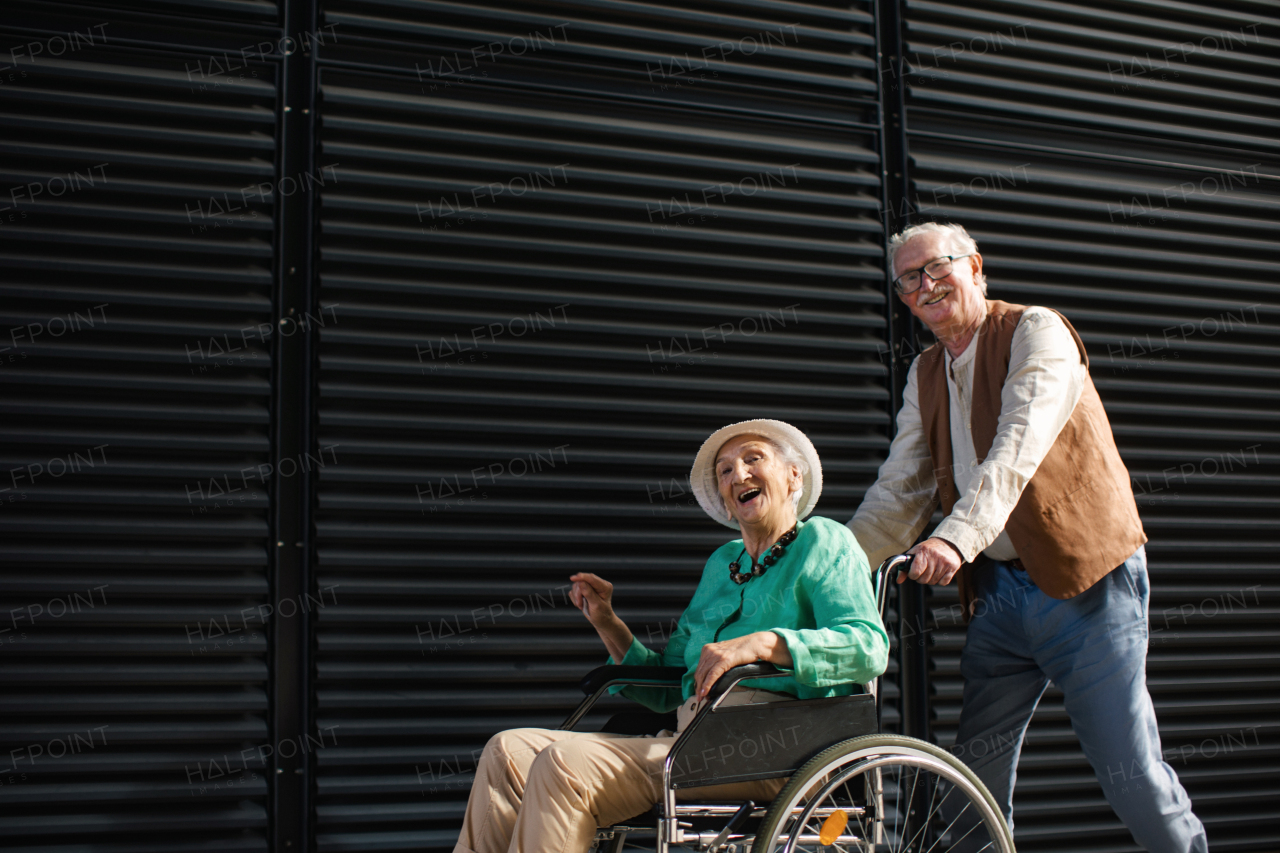 Portrait of senior couple with woman in wheelchair. Elderly man pushing his lovely wife in wheelchair. Concept of chronic illness in elderly couple. Portrait with copy space on black background. Senior siblings on a Sunday stroll in the city.