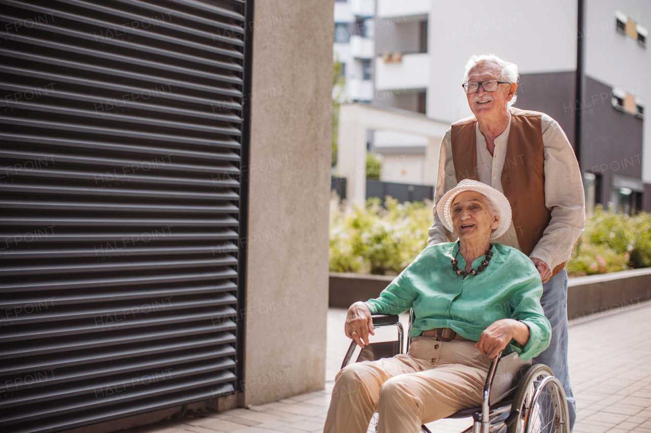 Portrait of senior couple with woman in wheelchair. Elderly man pushing his lovely wife in wheelchair. Concept of chronic illness in elderly couple. Portrait with copy space on black background. Senior siblings on a Sunday stroll in the city.