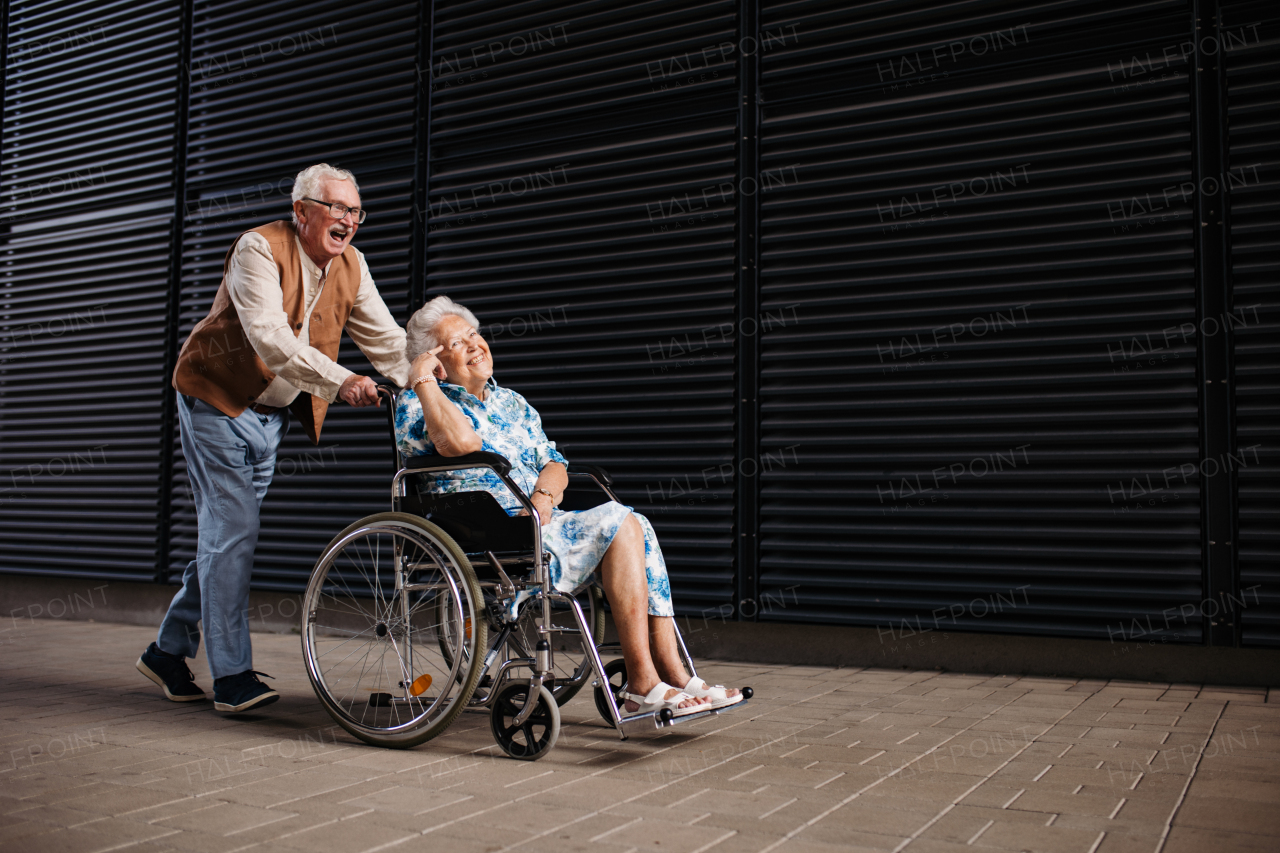 Portrait of senior couple with woman in wheelchair. Elderly man pushing his smiling wife in wheelchair. Concept of chronic illness in elderly couple. Portrait with copy space on black background.