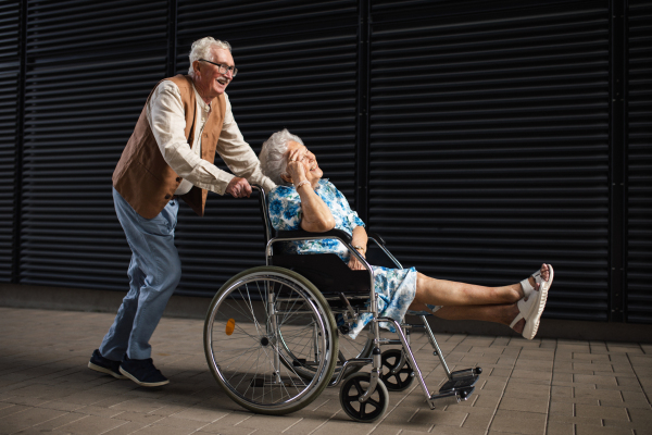 Portrait of senior couple with woman in wheelchair. Elderly man pushing his disabled wife in wheelchair. Concept of chronic illness in elderly couple. Portrait with copy space on black background.