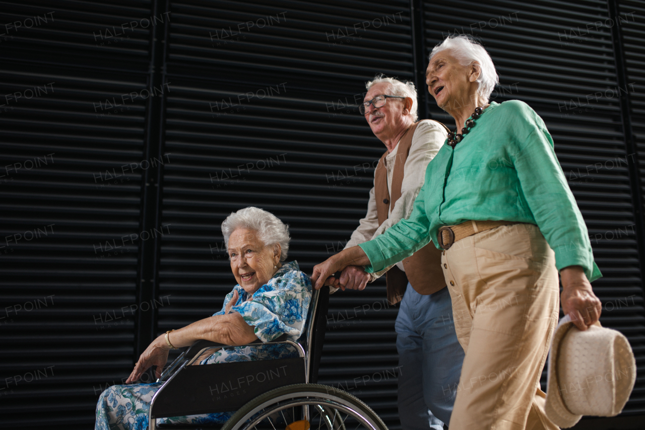 Portrait of group of senior friends with woman in wheelchair. Elderly friends pushing senior woman in wheelchair. Concept of chronic illness in elderly couple. Portrait with copy space on black background.