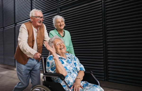 Portrait of group of senior friends with woman in wheelchair. Elderly friends pushing senior woman in wheelchair. Concept of chronic illness in elderly couple. Portrait with copy space on black background.