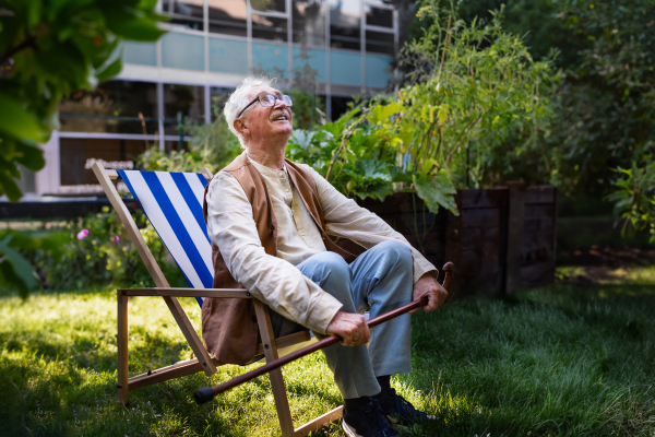 Portrait of smiling senior man resting after taking care vegetable plants in urban garden. Urban gardening in community garden making pensioner happy and cures his depression.