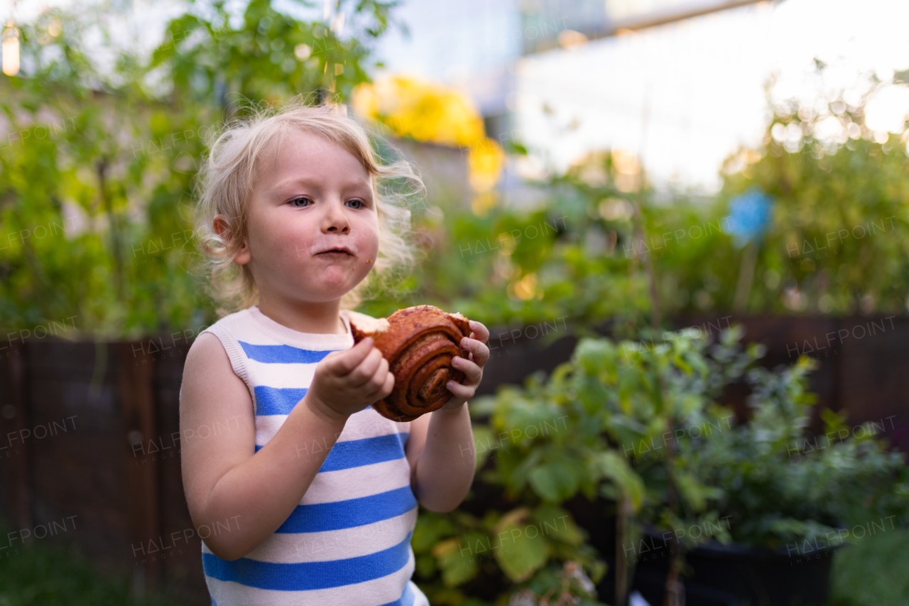 Little girl is eating a cinnamon roll outside in the garden. Sweet snack during a break while working in the garden.