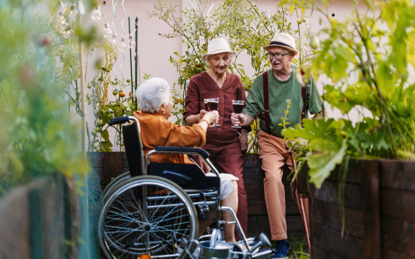 Portrait of senior friends relaxing, having glass of wine after hard work in urban garden in the city. Pensioners spending time together gardening in community garden in their apartment complex.