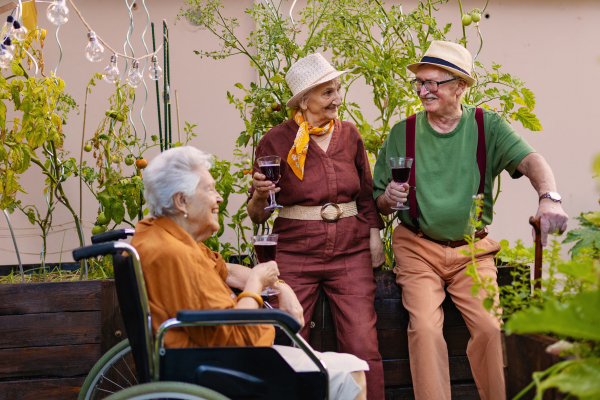 Portrait of senior friends relaxing, having glass of wine after hard work in urban garden in the city. Pensioners spending time together gardening in community garden in their apartment complex.