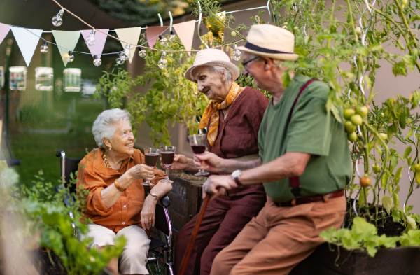 Portrait of senior friends relaxing, having glass of wine after hard work in urban garden in the city. Pensioners spending time together gardening in community garden in their apartment complex.