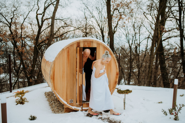 Senior woman in towel with her husband coming out from outdoor sauna during a cold winter day.