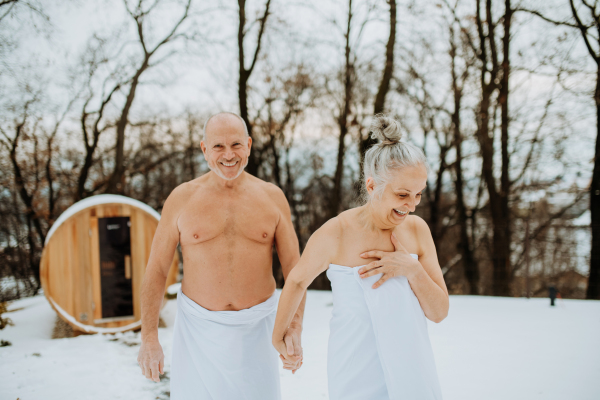 Senior woman in towel with her husband coming out from outdoor sauna during a cold winter day.