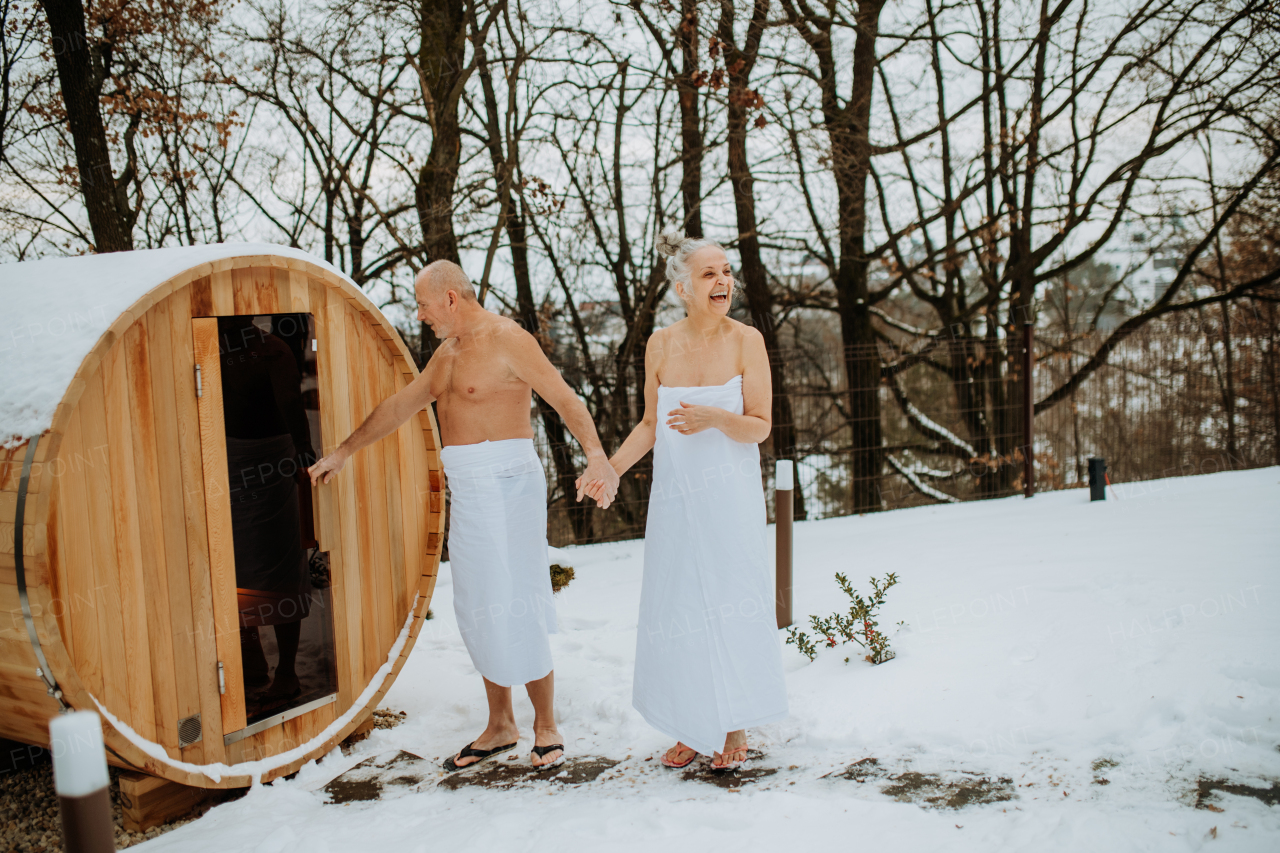 Senior woman in towel with her husband coming out from outdoor sauna during a cold winter day.