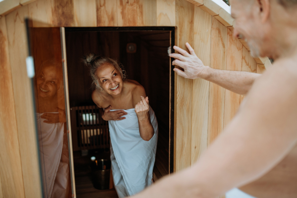 Senior woman in towel with her husband coming out from outdoor sauna during a cold winter day.