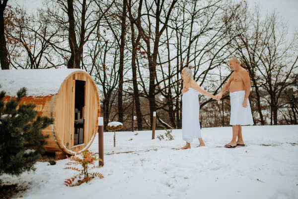 Senior woman in towel with her husband coming out from outdoor sauna during a cold winter day.