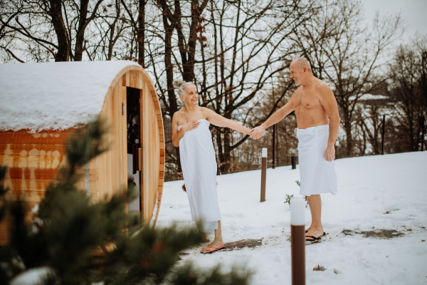 Senior woman in towel with her husband coming out from outdoor sauna during a cold winter day.