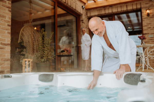 Senior man in a bathrobe checking temperature in outdoor hot tub, preparing for bathing with his wife.