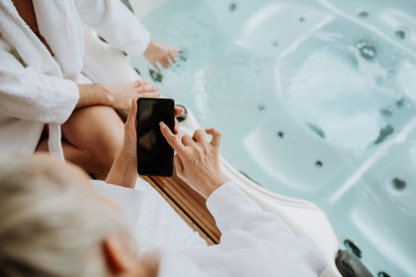 Top view of senior couple setting outdoor bathtub with smartphone.