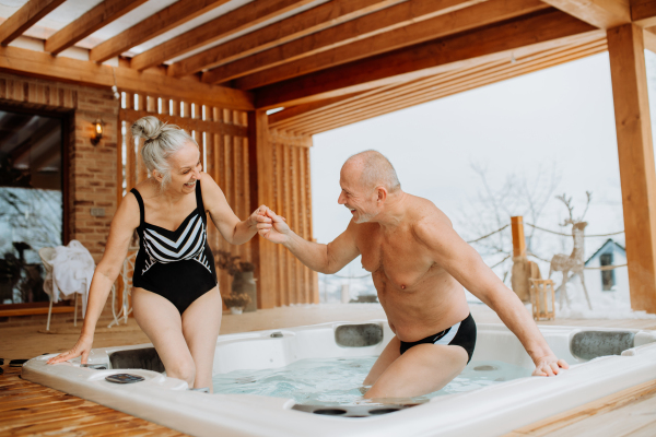 Senior couple enterying in outdoor bathtub at their terrace, during a cold winter day.