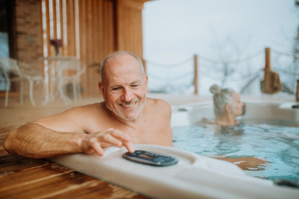 Senior couple enjoying together outdoor bathtub at their terrace during a cold winter day.