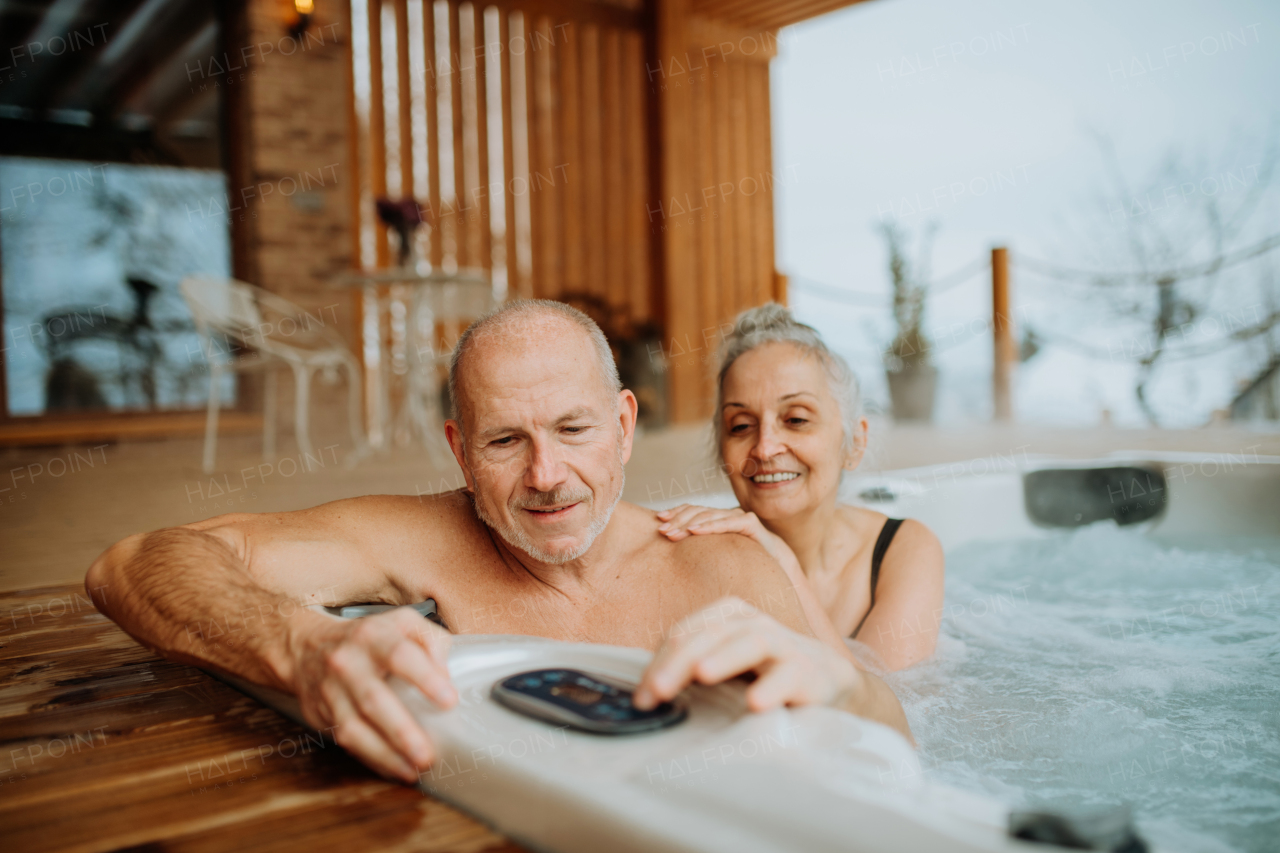 Senior couple enjoying together outdoor bathtub at their terrace during a cold winter day.