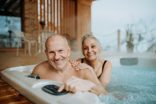 Senior couple enjoying together outdoor bathtub at their terrace during a cold winter day.