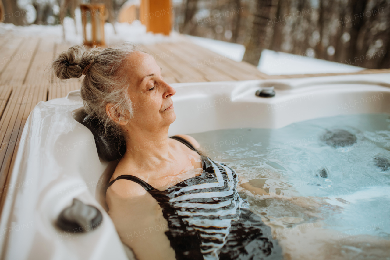 Senior woman enjoying outdoor bathtub at terrace during a cold winter day.