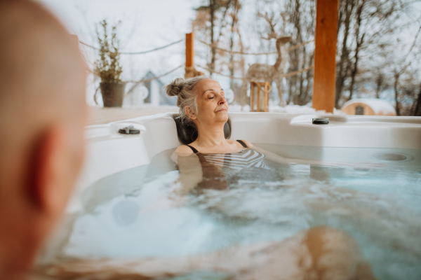 Senior woman enjoying outdoor bathtub with her husband at terrace during a cold winter day.