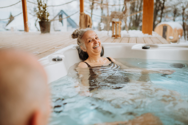 Senior woman enjoying outdoor bathtub with her husband at terrace during a cold winter day.