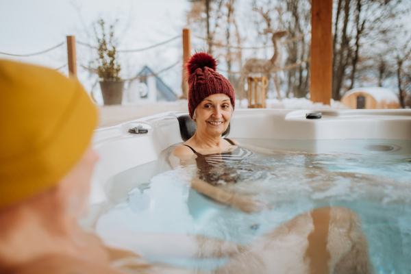 Senior couple in knitted cap enjoying together outdoor bathtub at their terrace during a cold winter day.