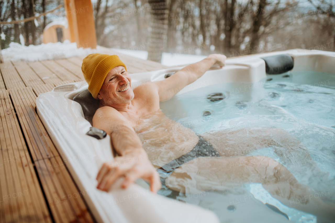 Senior man enjoying outdoor bathtub at terrace during a cold winter day.