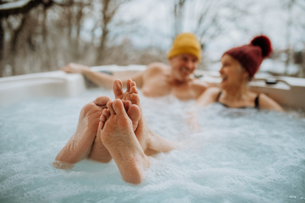 Senior couple in knitted cap enjoying together outdoor bathtub at their terrace during a cold winter day.