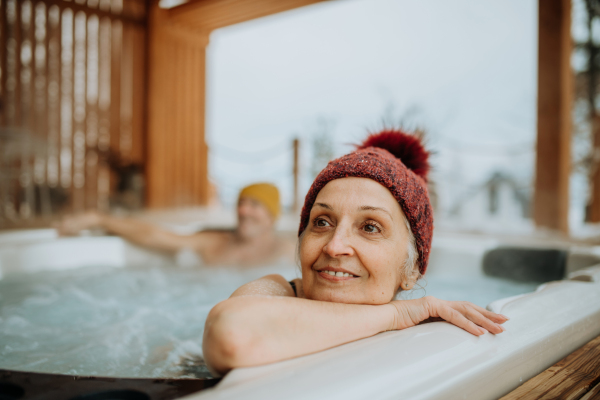 Senior woman enjoying outdoor bathtub at terrace during a cold winter day.