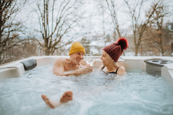 Senior couple in knitted cap enjoying together outdoor bathtub at their terrace during a cold winter day.