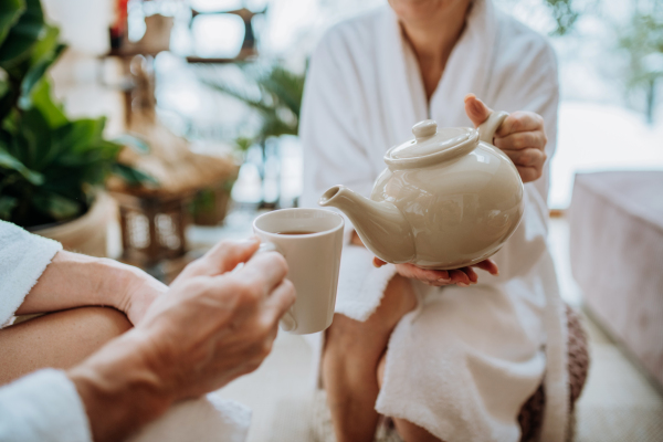 Close-up of senior couple in bathrobes pouring a hot tea, calm and hygge atmosphere.