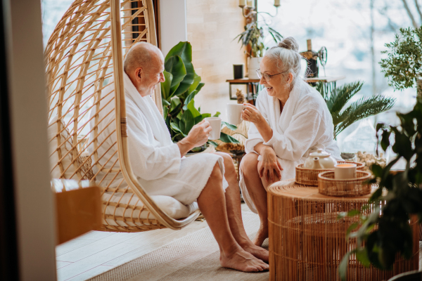 Senior couple in bathrobes enjoying time together in their living room, drinking a hot tea, calm and hygge atmosphere.