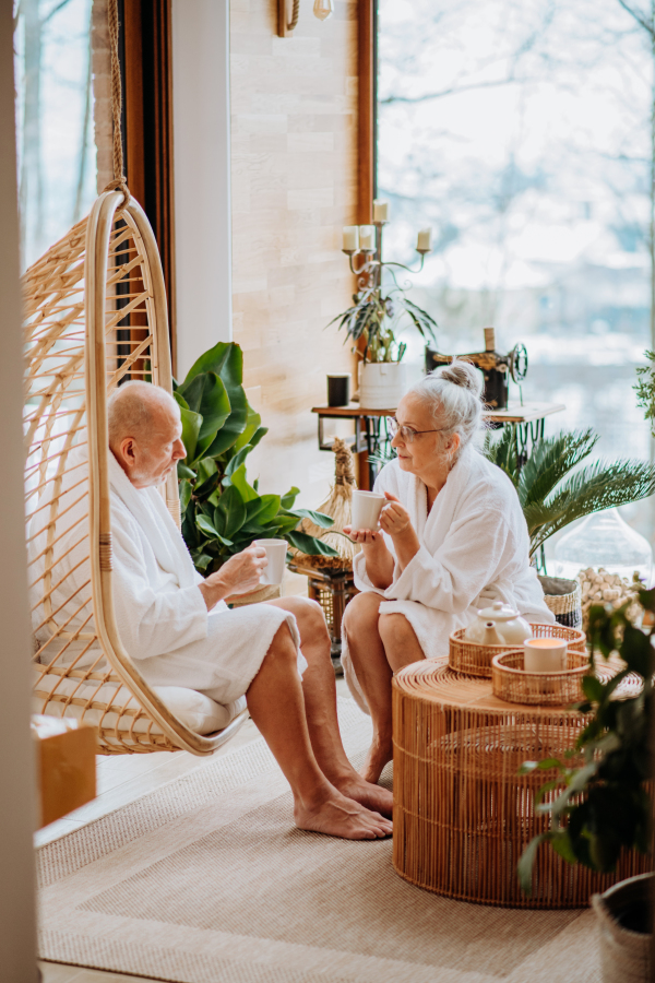 Senior couple in bathrobes enjoying time together in their living room, drinking a hot tea, calm and hygge atmosphere.