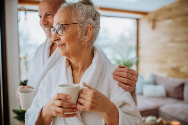 Senior couple in bathrobes enjoying time together in their living room, drinking a hot tea, calm and hygge atmosphere.