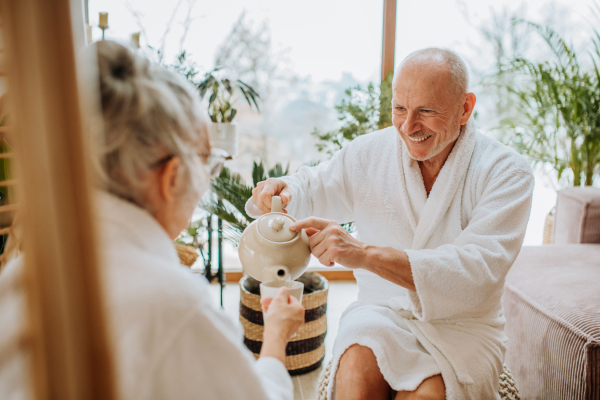 Senior couple in bathrobes enjoying time together in their living room, drinking a hot tea, calm and hygge atmosphere.