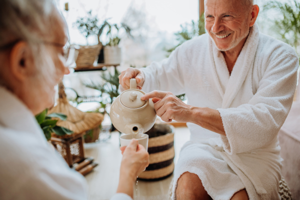 Senior couple in bathrobes enjoying time together in their living room, drinking a hot tea, calm and hygge atmosphere.